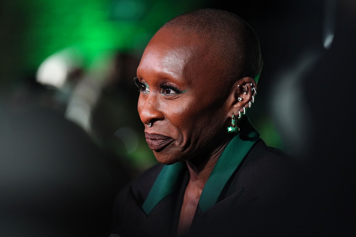 Cynthia Erivo styles her green outfit with emerald and jadeite earrings by Dyne, a few diamond hoop earrings, and statement rings