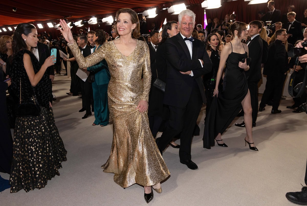 Sigourney Weaver shimmered across the champagne-colored Oscars carpet in a custom metallic gold Givenchy gown, styled with sleek black pointed-toe pumps that added a grounded contrast to the dramatic leopard-patterned fabric