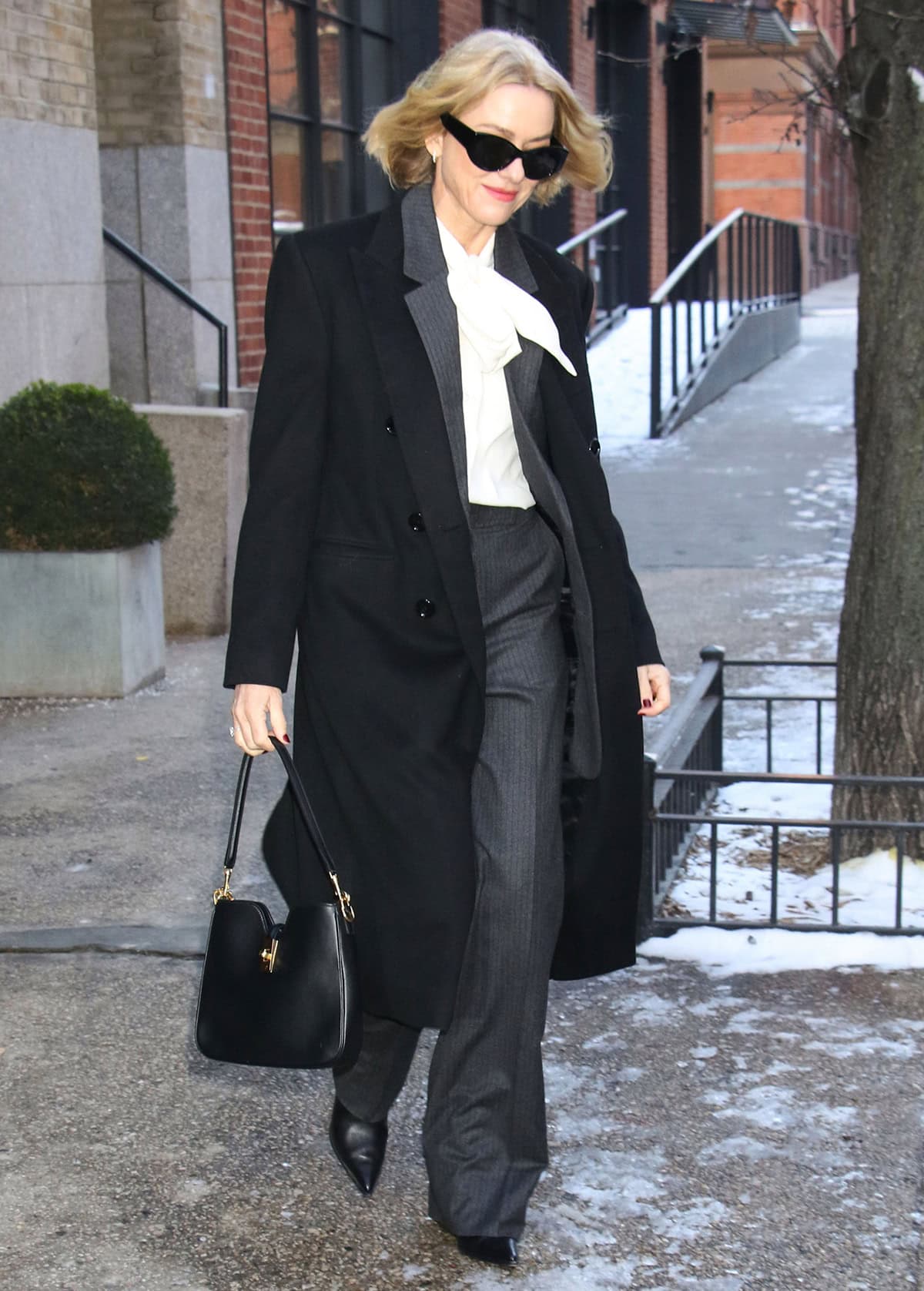 Naomi Watts power dresses with a gray pinstripe suit by Celine, a white Lavallière blouse, and a black coat