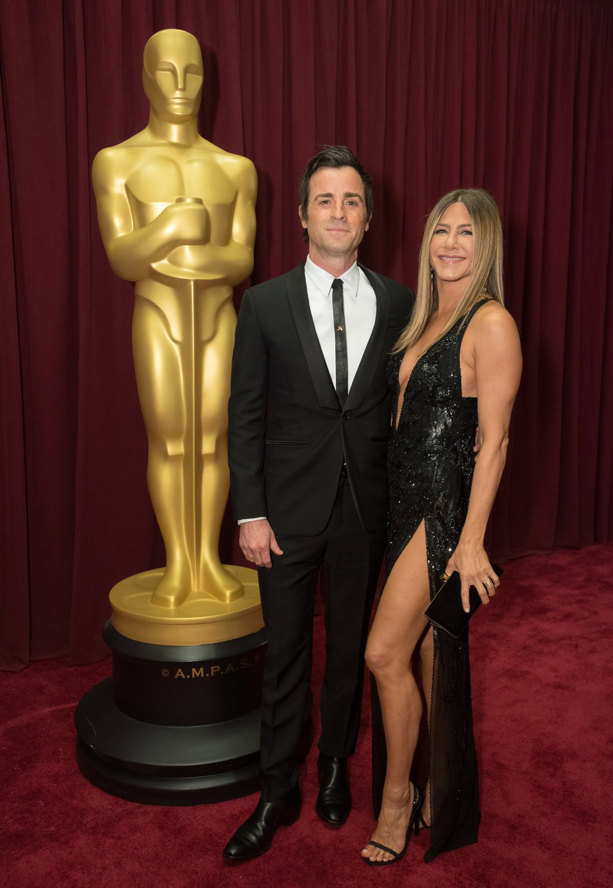 Jennifer Aniston balances the daring thigh-high slit of her black sequined Atelier Versace gown with minimalist Gucci “Mallory” stiletto sandals, creating the elongated, leg-lengthening silhouette that defines her signature red-carpet style alongside Justin Theroux at the 89th Academy Awards