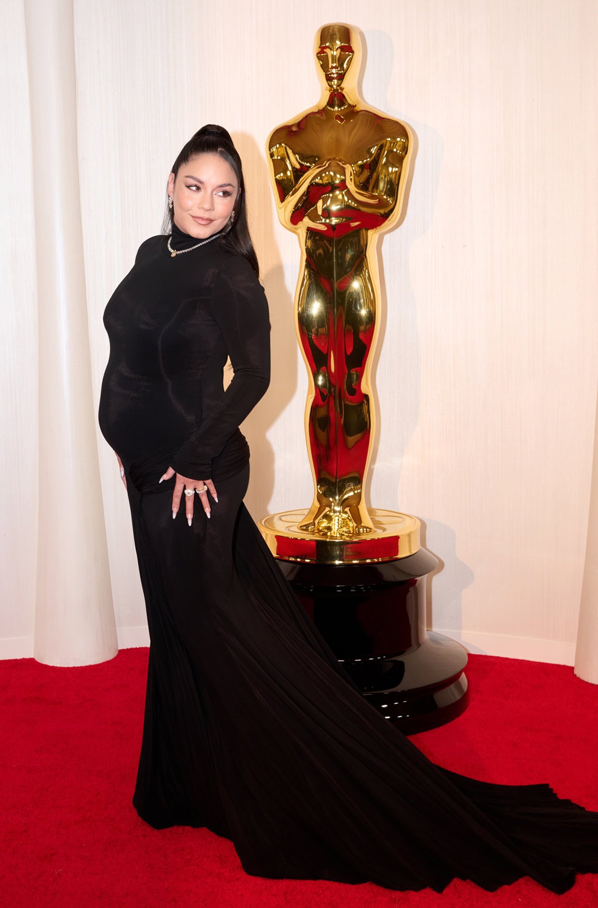 Vanessa Hudgens showcased understated Oscars glamour in a figure-skimming black gown with a dramatic train, using sleek styling and hidden heels to elegantly accentuate her petite 5-foot-1 frame at the 2024 Academy Awards