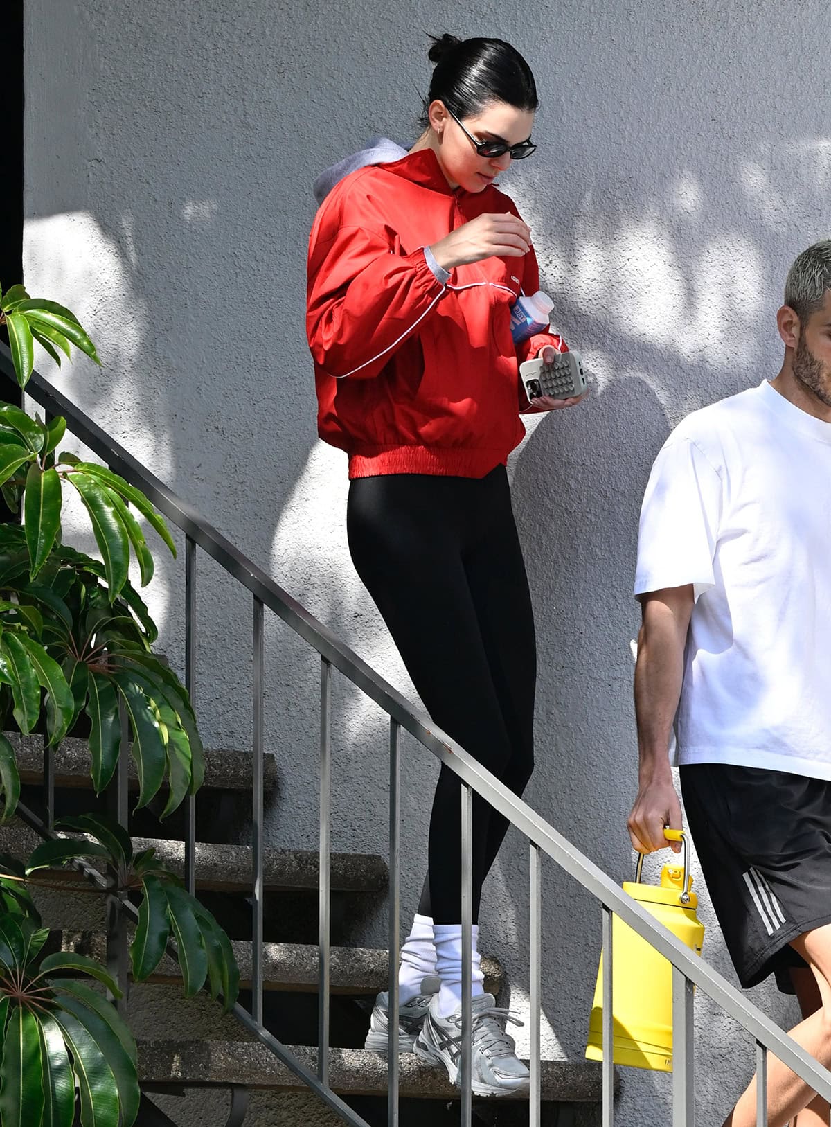 Kendall Jenner looks chic in black leggings with a vibrant red track jacket by Adanola and a gray hoodie underneath