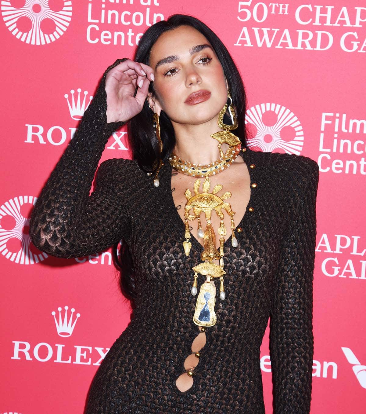 Dua Lipa accessorizes her already striking mesh dress with Schiaparelli's statement Keyhole earrings and bib necklace with a deconstructed face featuring the house's signature Eye, Nose, and Mouth