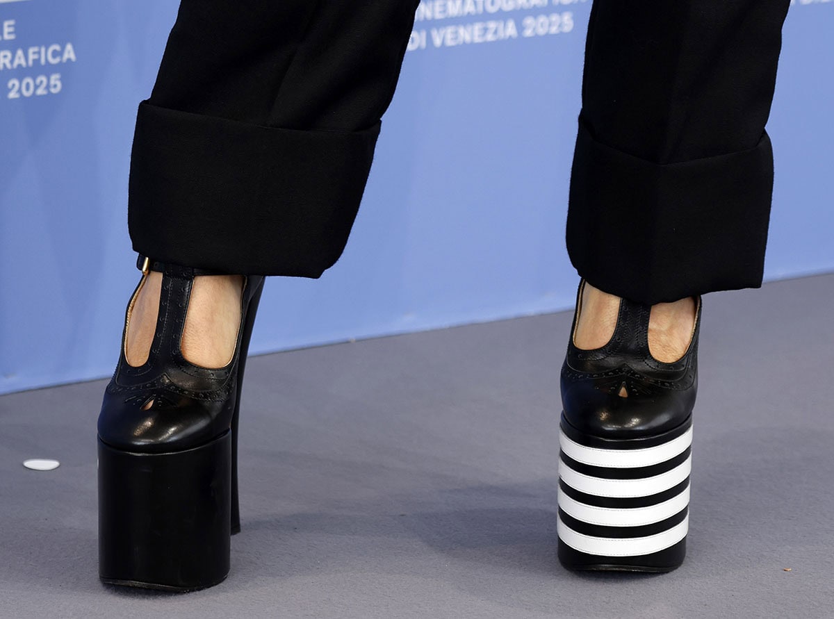 Rebecca Ferguson completes her sleek, tailored look with Thom Browne's brogue-style pumps, featuring a perforated T-strap and round toe, towering block heels, and mismatched plain and striped platforms