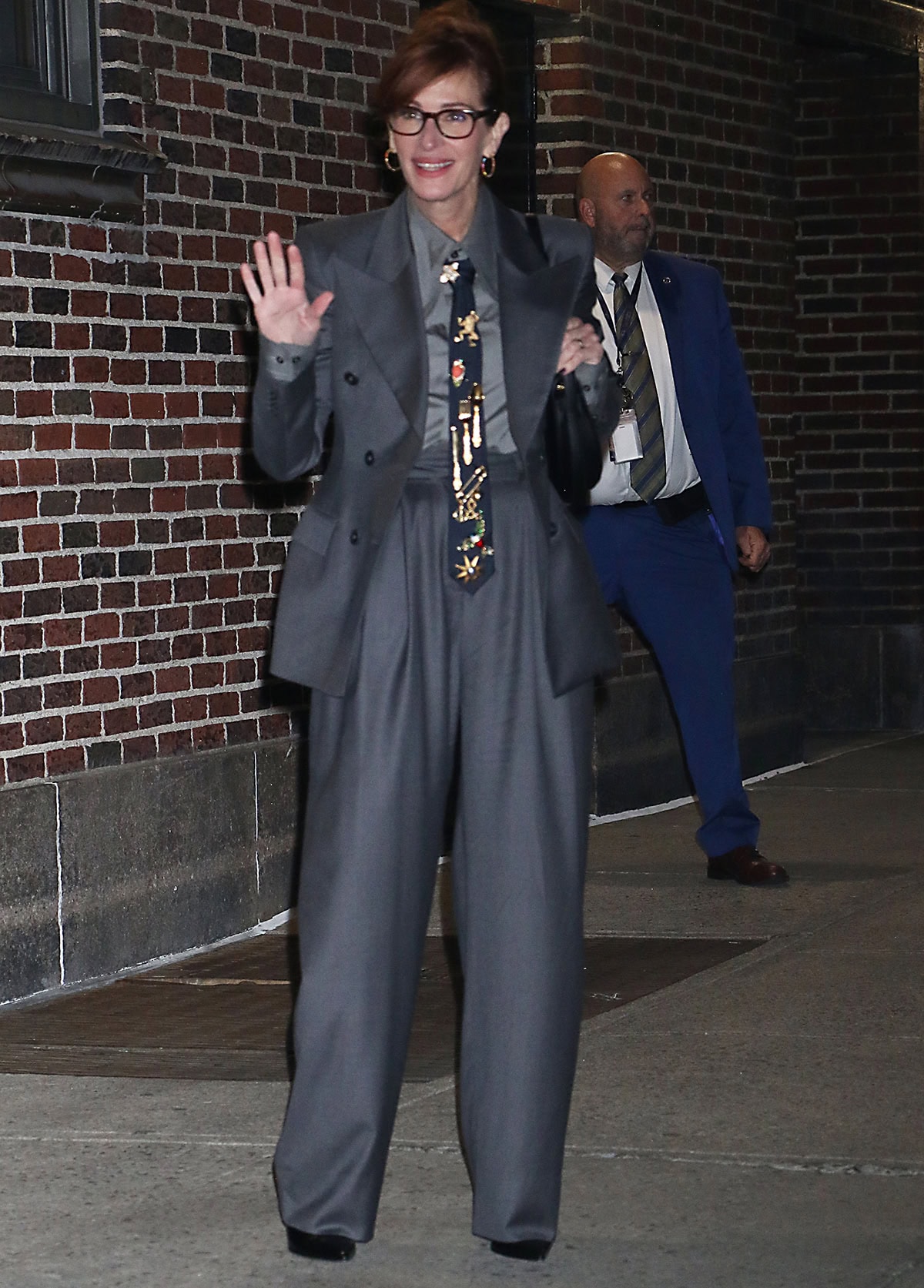 Julia Roberts channels timeless menswear elegance in a gray Salon 1884 suit with a peaked-lapel blazer, pleated wide-leg trousers, and a vintage brooch-adorned tie for her appearance on The Late Show with Stephen Colbert on October 1, 2025, in New York City