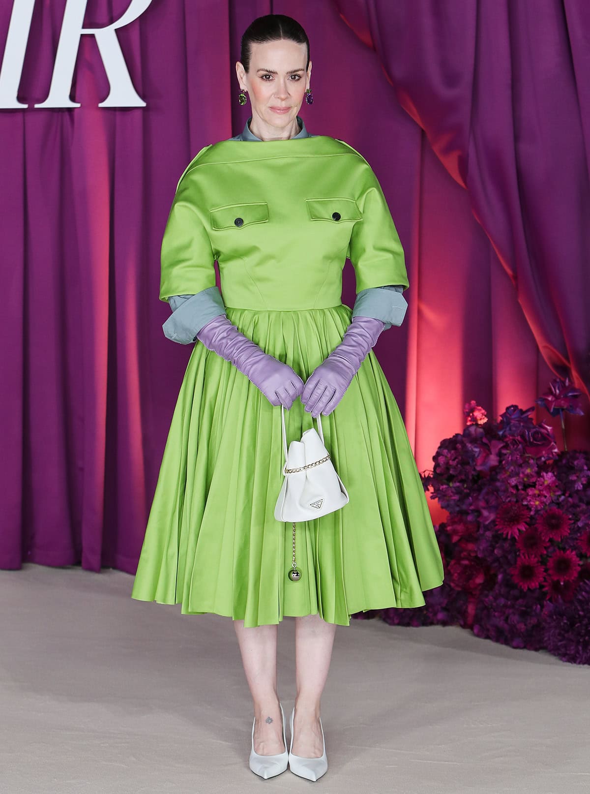 Sarah Paulson steals the spotlight in a lime-green A-line midi dress by Prada, featuring a boxy bodice with chest pockets, epaulets, and a feminine pleated skirt