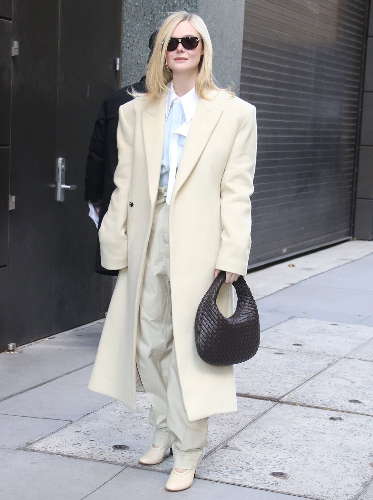 Elle Fanning embraces soft power dressing in a creamy Bottega Veneta coat, matching trousers with a tie waist, and a light blue shirt with a white collar outside the Live With Kelly Mark studios