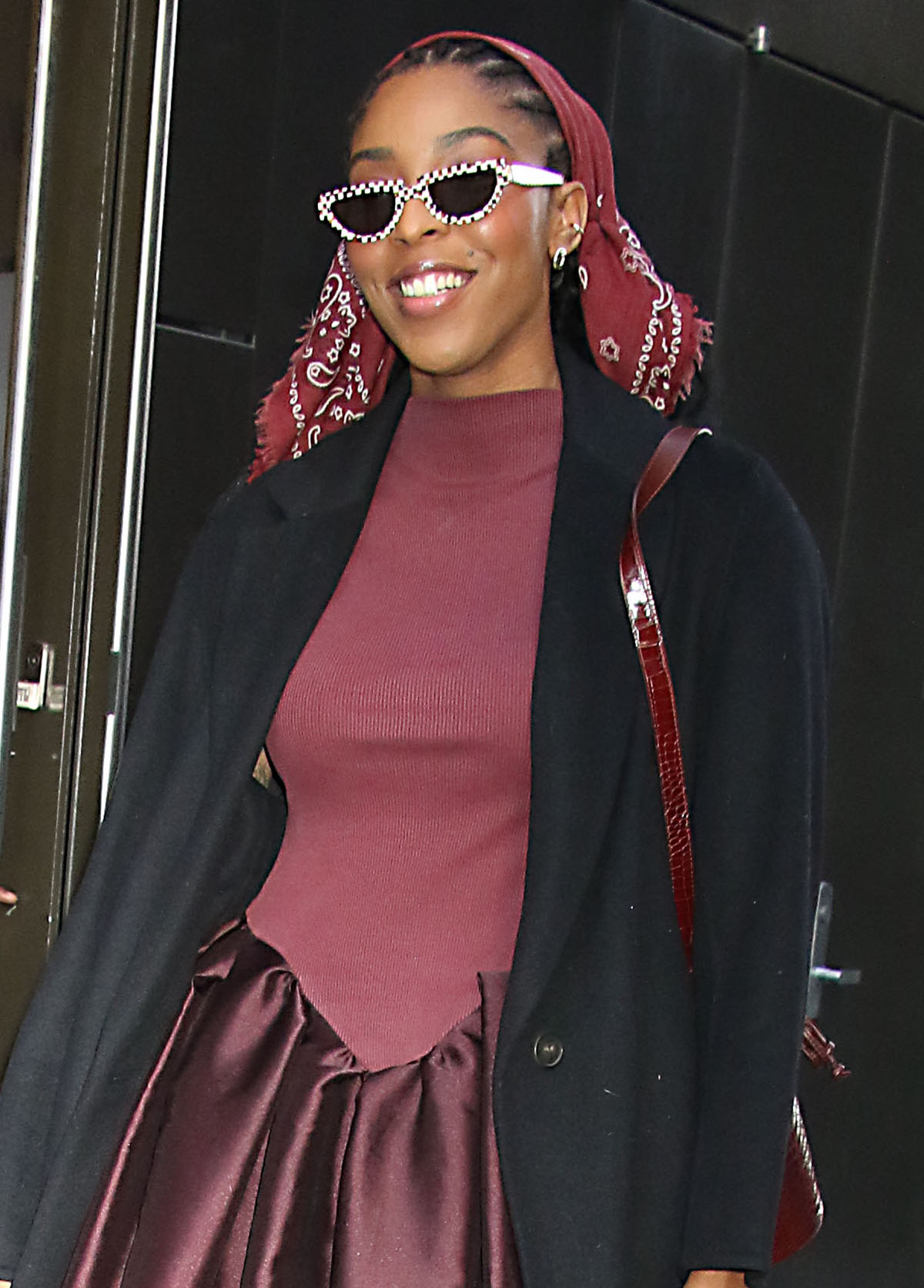 Jessica Williams styles her look with a burgundy bandana, white pixel-printed sunnies, and a burgundy croc-embossed bucket bag