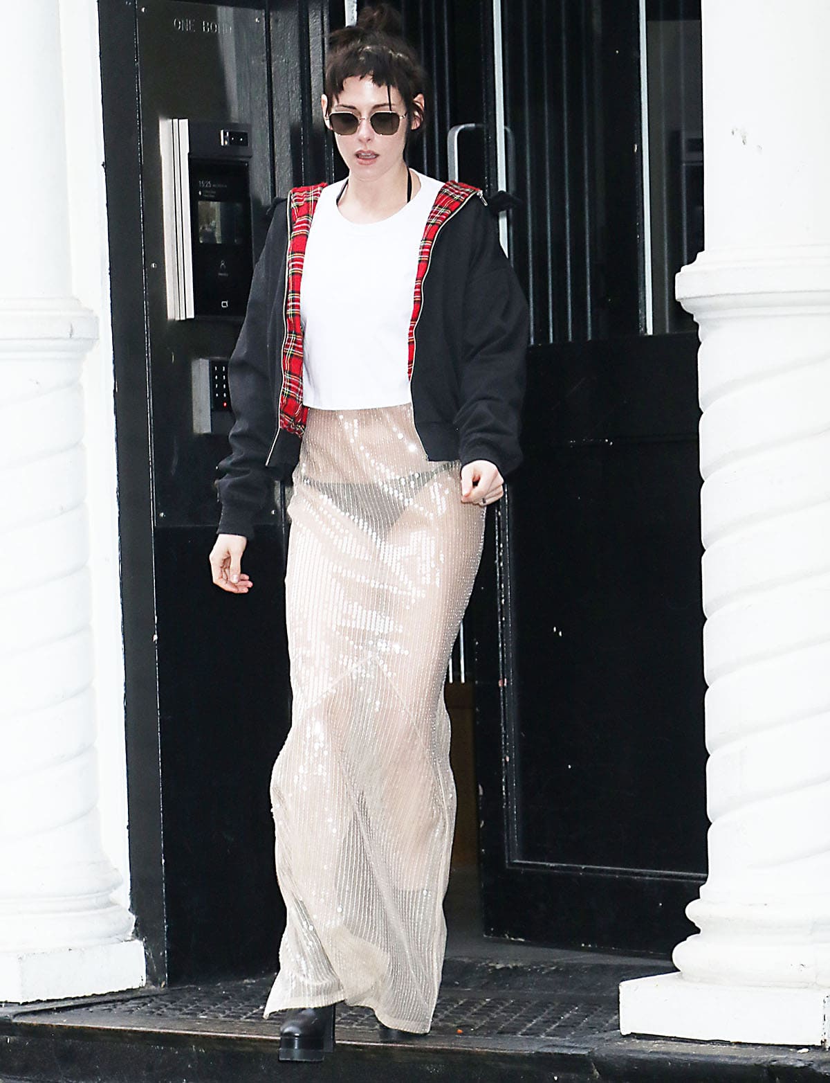 Kristen Stewart wears The New Arrivals Ilkyaz Ozel “Isis” maxi dress, featuring a beige see-through material embellished with shimmering sequins, with a white Leset crop top and a black jacket with a red plaid lining
