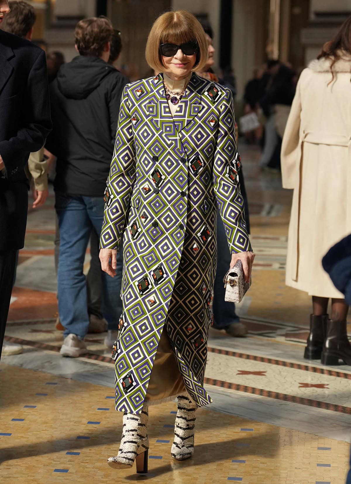 Anna Wintour pairs her snakeskin boots with a geometric-patterned archival Prada coat in green, purple, and white, with metal embellishments, amber and black crystal rhinestones, and plexi shapes