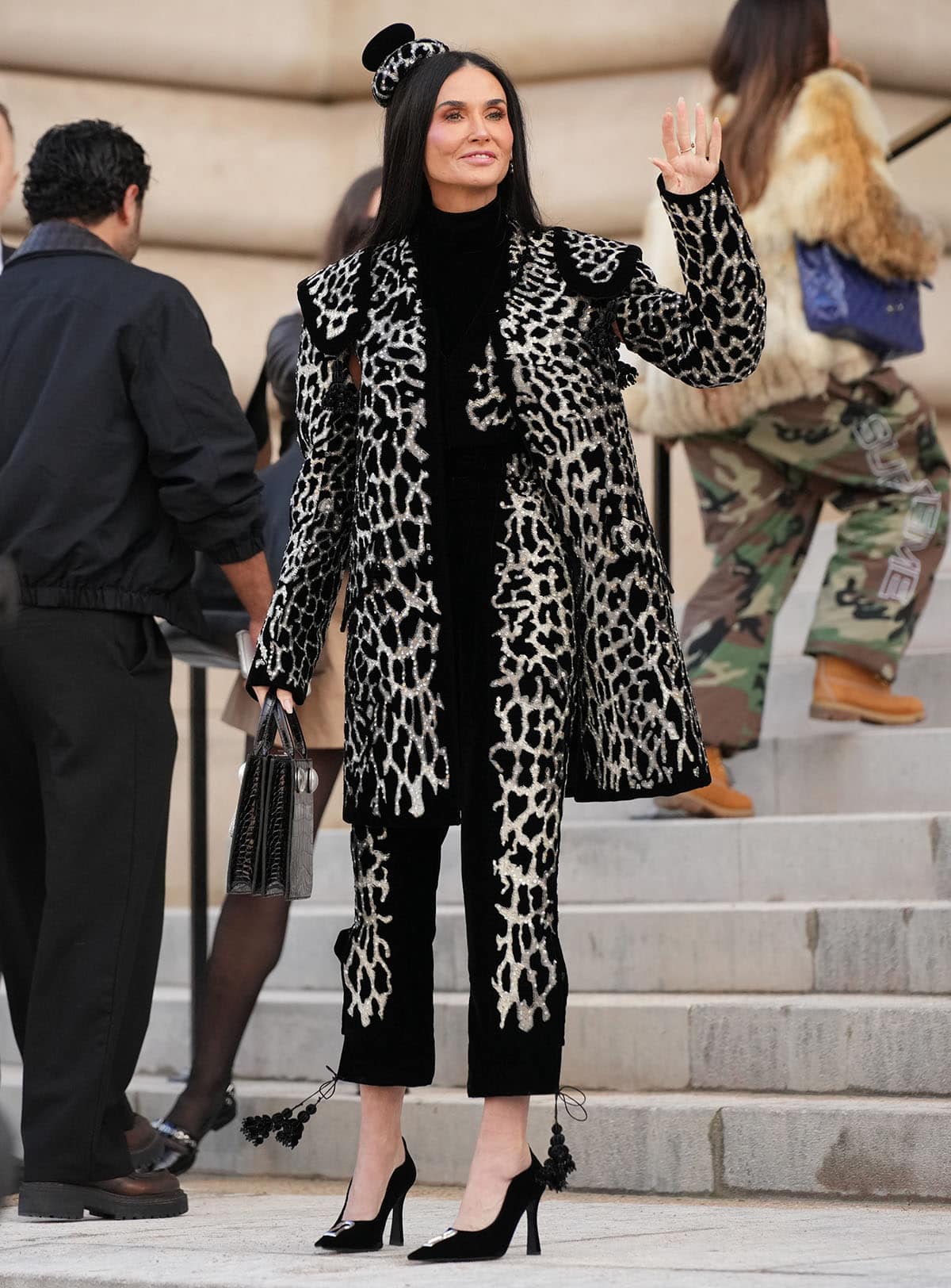 Demi Moore pairs her pumps with a black velvet outfit, featuring a turtleneck top, a vest, torero pants, and a coat with saddle-inspired shoulders, all embroidered with a shimmering leopard pattern
