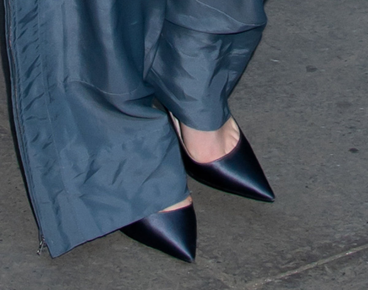 Dove Cameron finishes her modern tailoring with sleek satin pointed-toe pumps, their sharp silhouette and subtle sheen echoing the cool tones of her fluid gray trousers