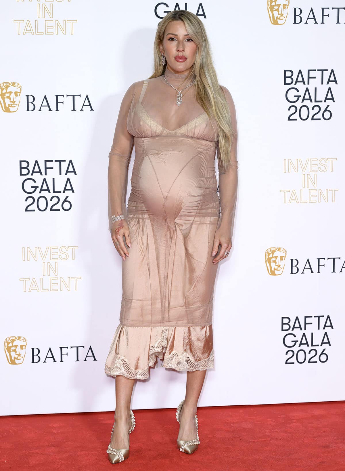 Ellie Goulding proudly shows off her baby bump in a blush pink slip dress with white lace trims and a sheer overlay