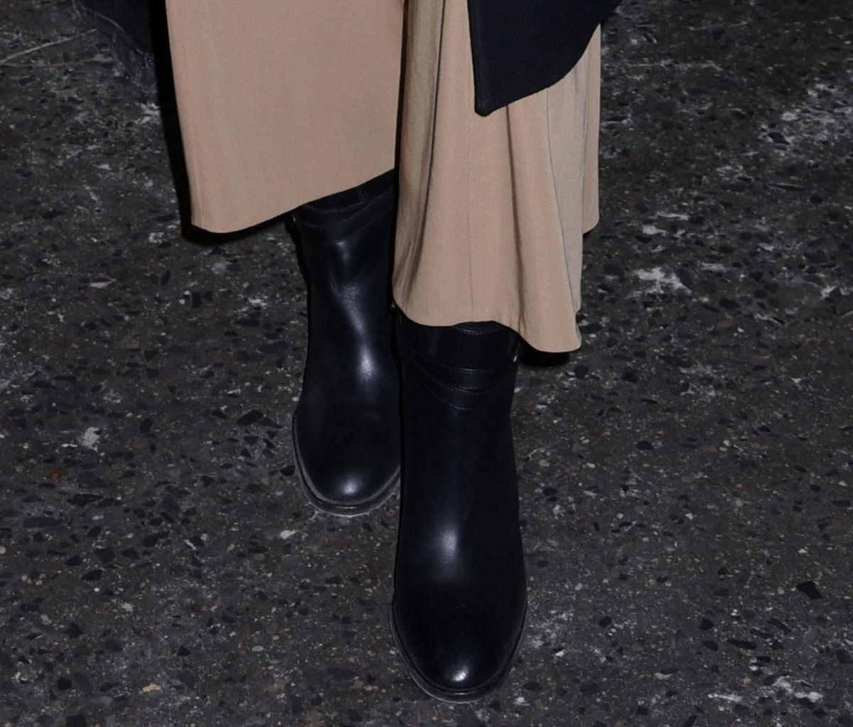 Emilia Jones adds a subtly edgy finish to her look in sleek black rounded-toe boots, defined by wraparound ankle straps and a high heel that brings polish and attitude in equal measure