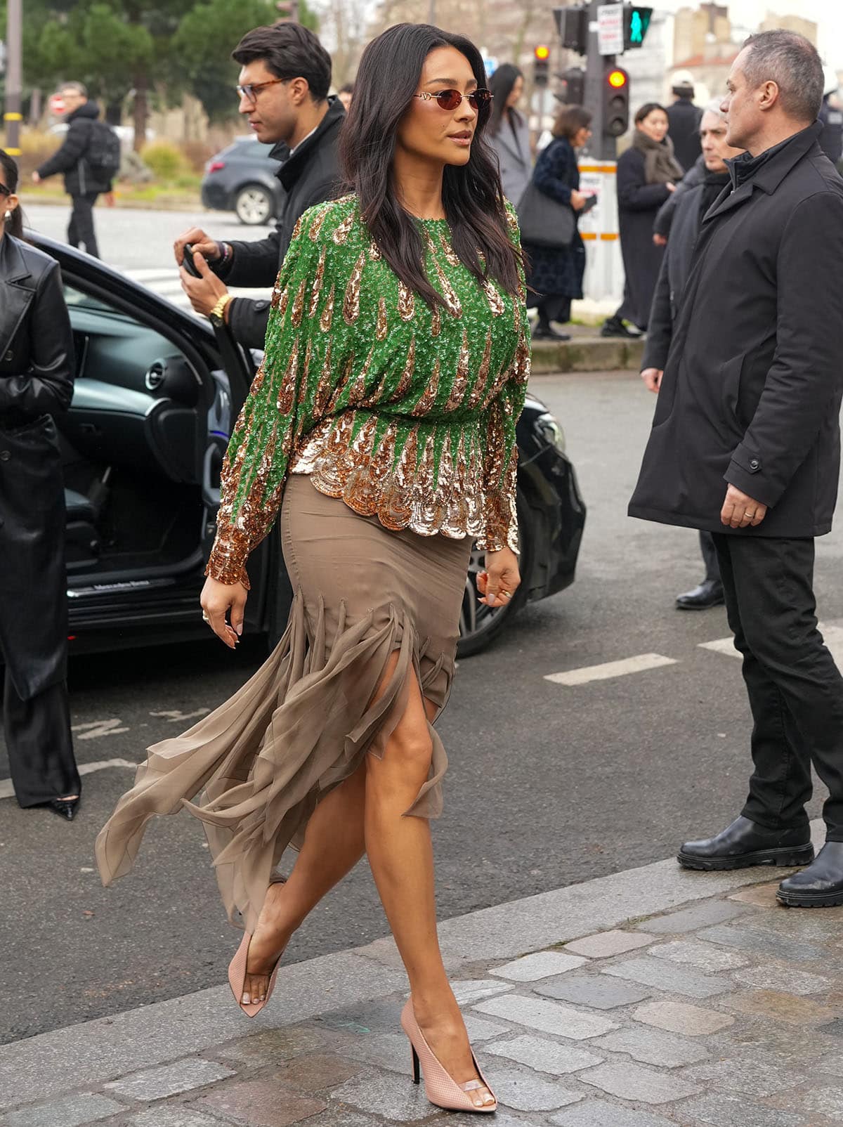 Shay Mitchell pairs her beige shoes with a sequined green and gold blouse and a semi-sheer khaki mini skirt with dangling handkerchief tassels