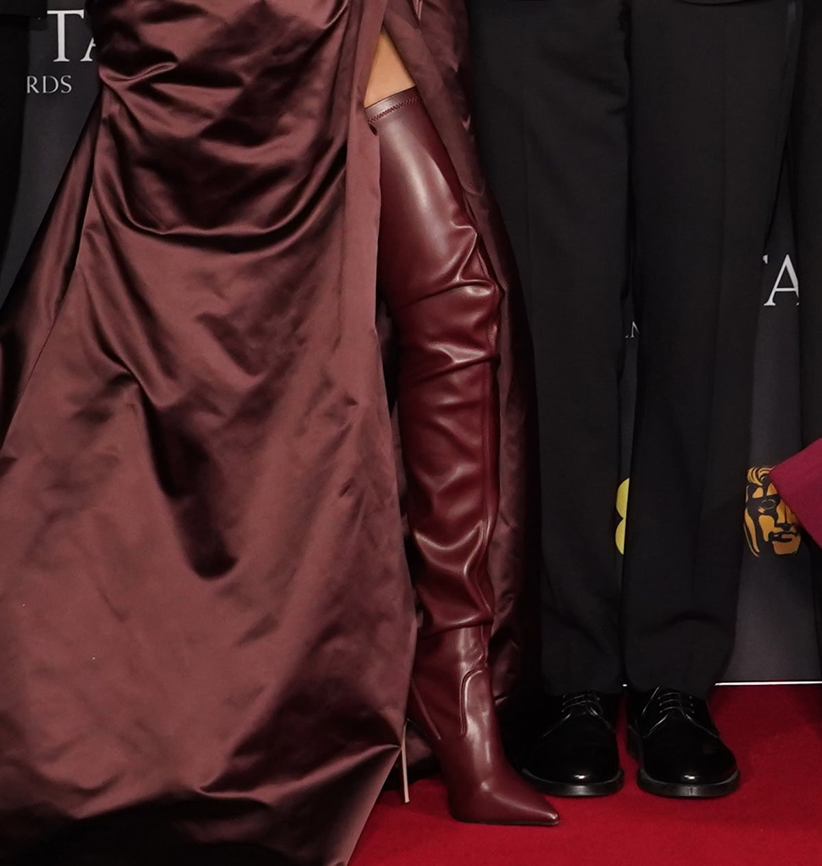 Teyana Taylor makes a strong entrance in Le Silla “Eva” thigh-high boots in cherry red vegan leather with slouchy shafts, pointed toes, and stiletto heels