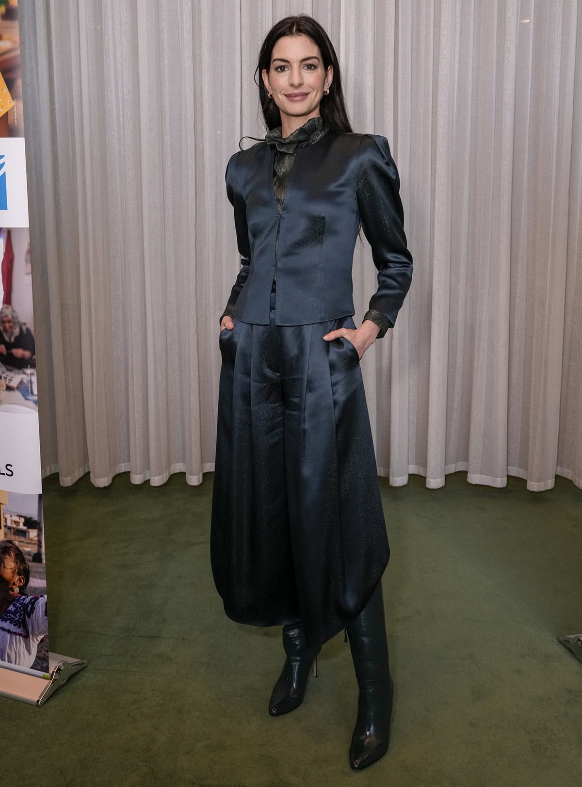 Anne Hathaway pairs her knee-high boots with a glittery navy satin jacket, a glittery ruffled high-neck blouse, and wide-leg crop trousers from Armani