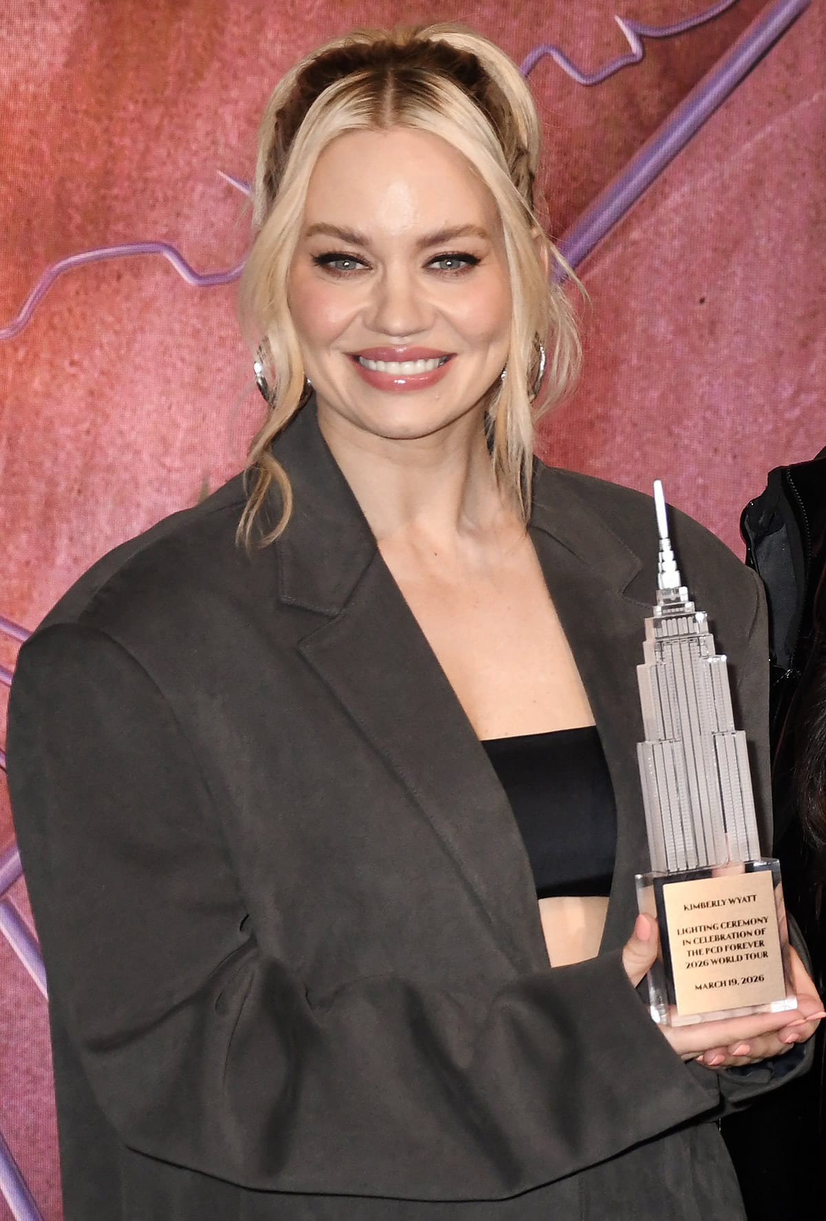 Kimberly Wyatt pairs her shiny boots with a gray suede shortsuit featuring an oversized blazer, a black bandeau underneath, and knee-length shorts