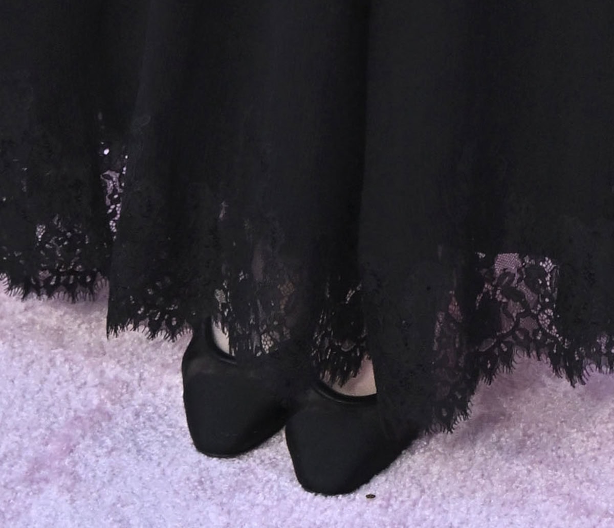 Sadie Sandler wears black mesh pumps with leather trims and cap toes, adding subtle texture and contrast beneath her lace-trimmed hem
