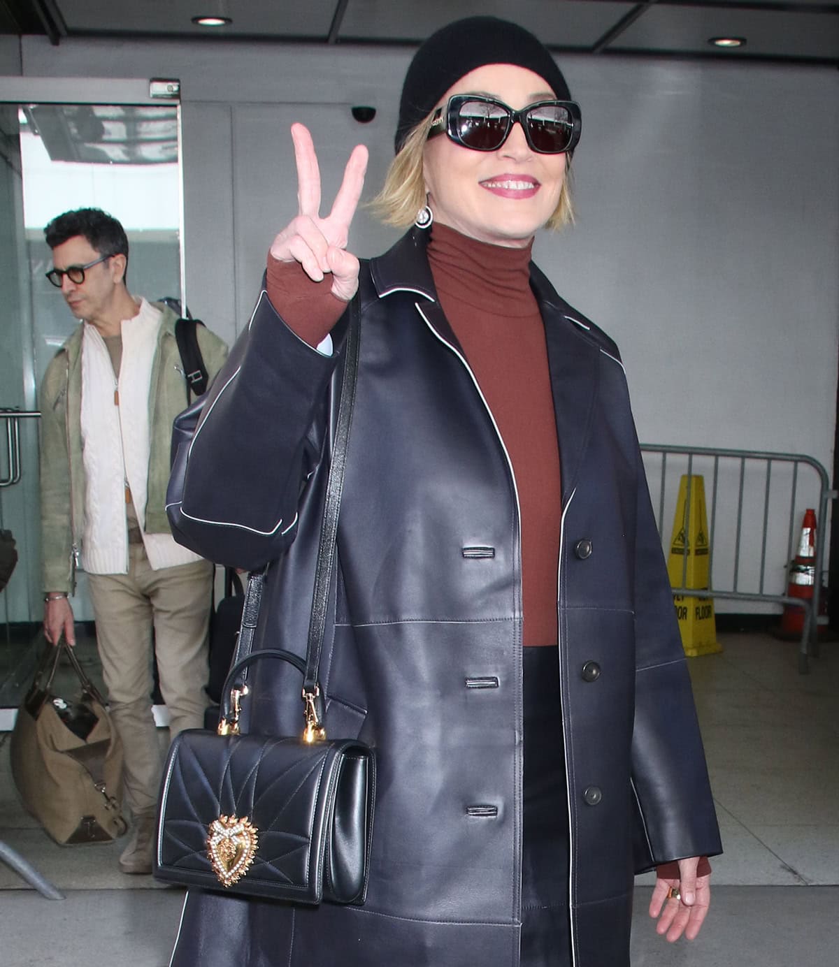 Sharon Stone styles her already bold ensemble with a Dolce Gabbana bag, a beanie, drop earrings, and black sunglasses