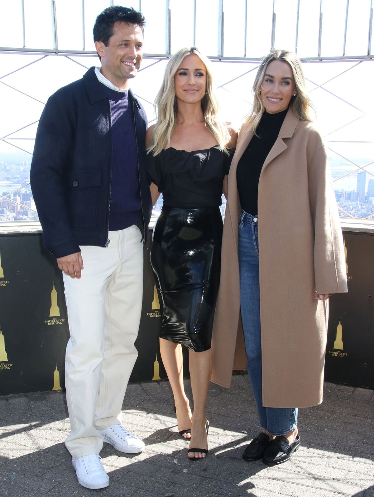 Kristin Cavallari sharpens her glossy PVC look with minimal black slingback heels, while Lauren Conrad keeps it effortless in black Rag Bone mules alongside Stephen Colletti’s clean white sneakers at the Empire State Building on April 7, 2026, in New York City