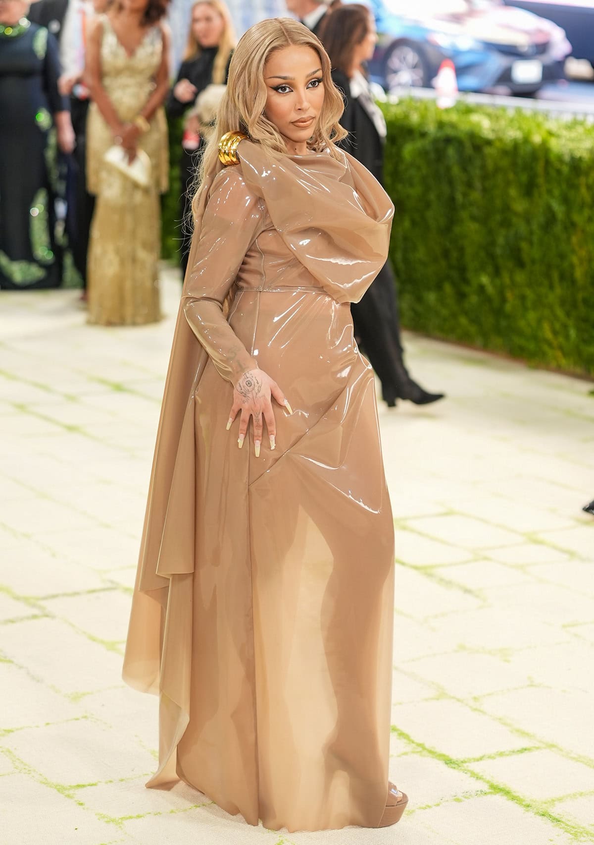 Doja Cat embraces cohesiveness, pairing her nude mules with a PVC-like silicone drape dress by Saint Laurent, blonde hair, and nude makeup