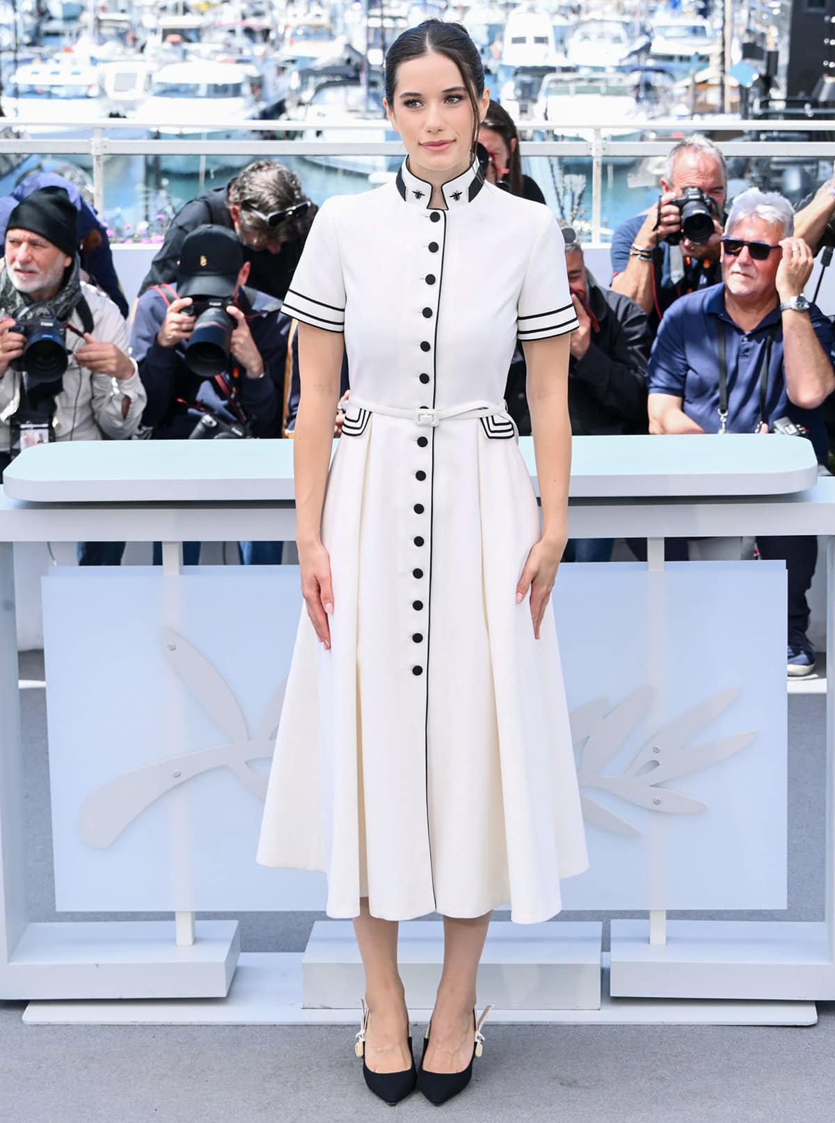 Ella Bleu Travolta pairs her pumps with a regal ecru wool and mohair midi dress by Dior, featuring a stand-up collar with bee embroideries, black buttons, a belted waist, and black stripes