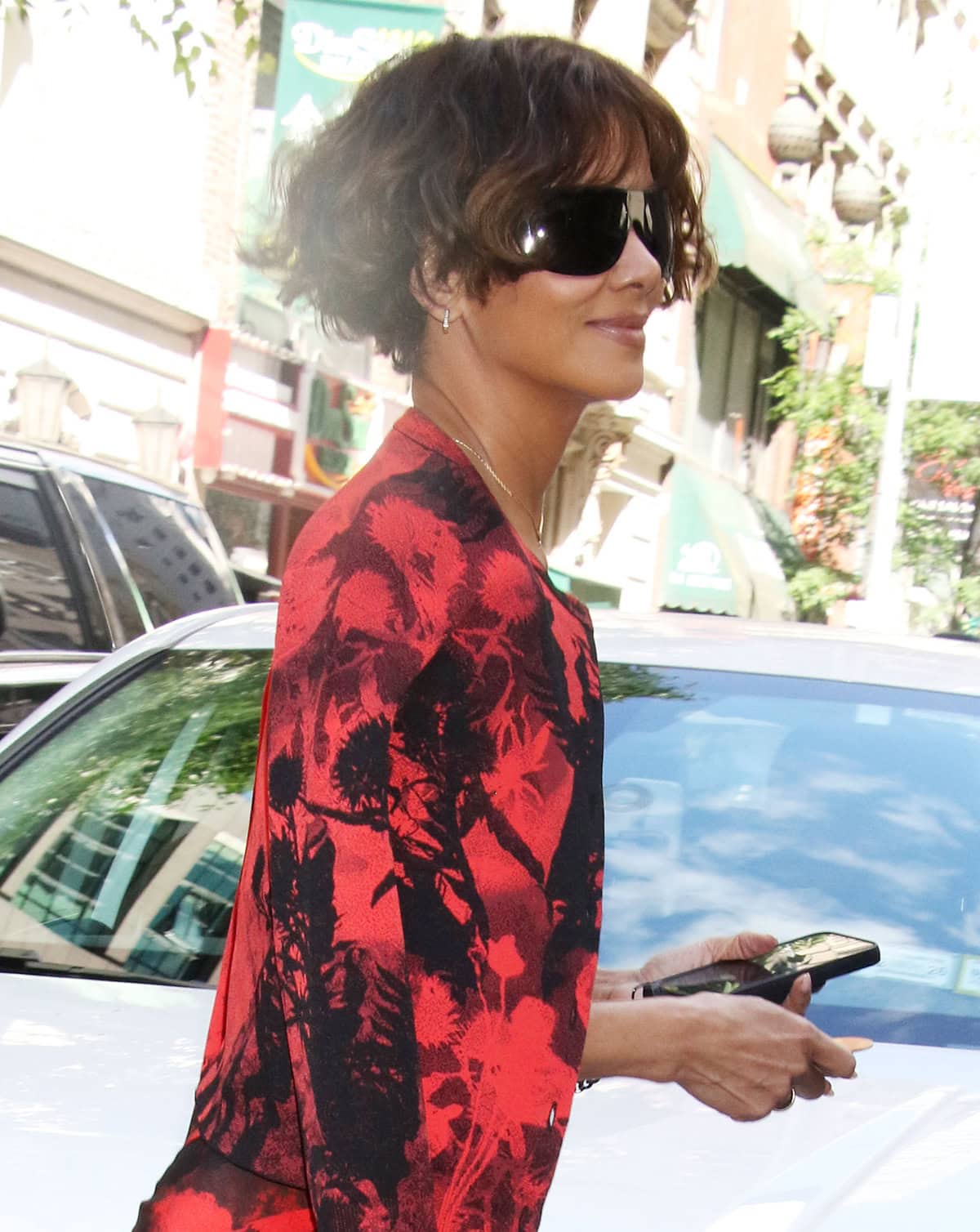 Halle Berry completes her fierce ensemble with oversized black sunnies, square hoop earrings, a lariat necklace, and a short, curly bob