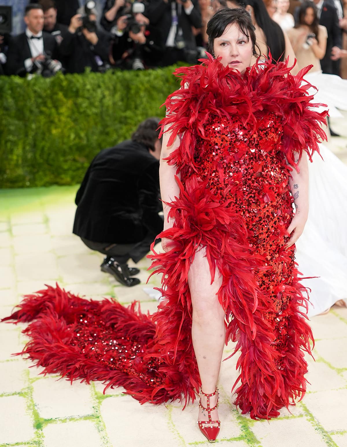Lena Dunham pairs her edgy red pumps with a strapless Valentino gown drenched in red sequins and trimmed with red feathers