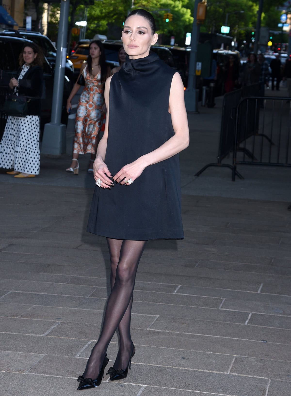 Olivia Palermo teams her bow slingback pumps with sheer tights and a sleeveless halter LBD with a draped neck by Khaite