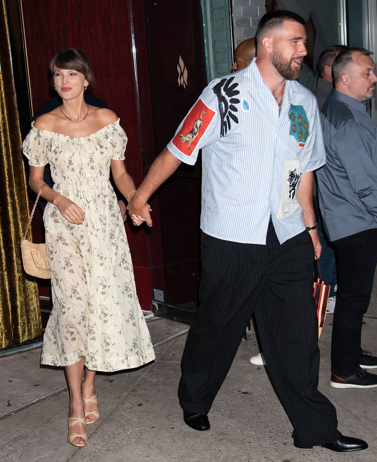 Taylor Swift teams her nude heels with a romantic floral dress by Dôen, featuring a smocked bodice with an off-the-shoulder ruffled neckline, short puff sleeves, and a flowy skirt, giving off a vintage countryside charm