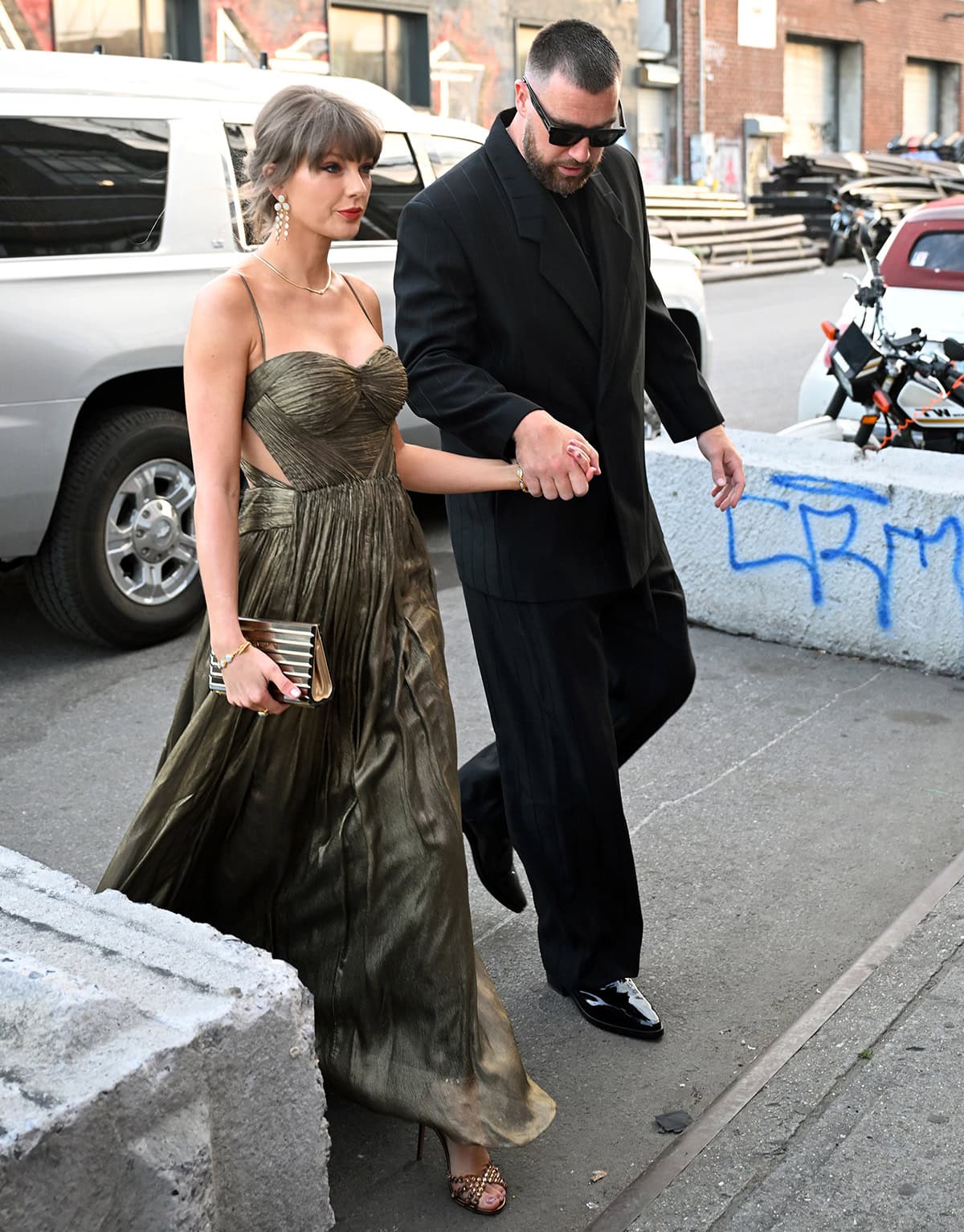 Taylor Swift pairs her metallic strappy sandals with a brushed gold Maria Lucia Hohan gown featuring a pleated construction, a bustier bodice, underwired cups, side cutouts, and an airy layered skirt