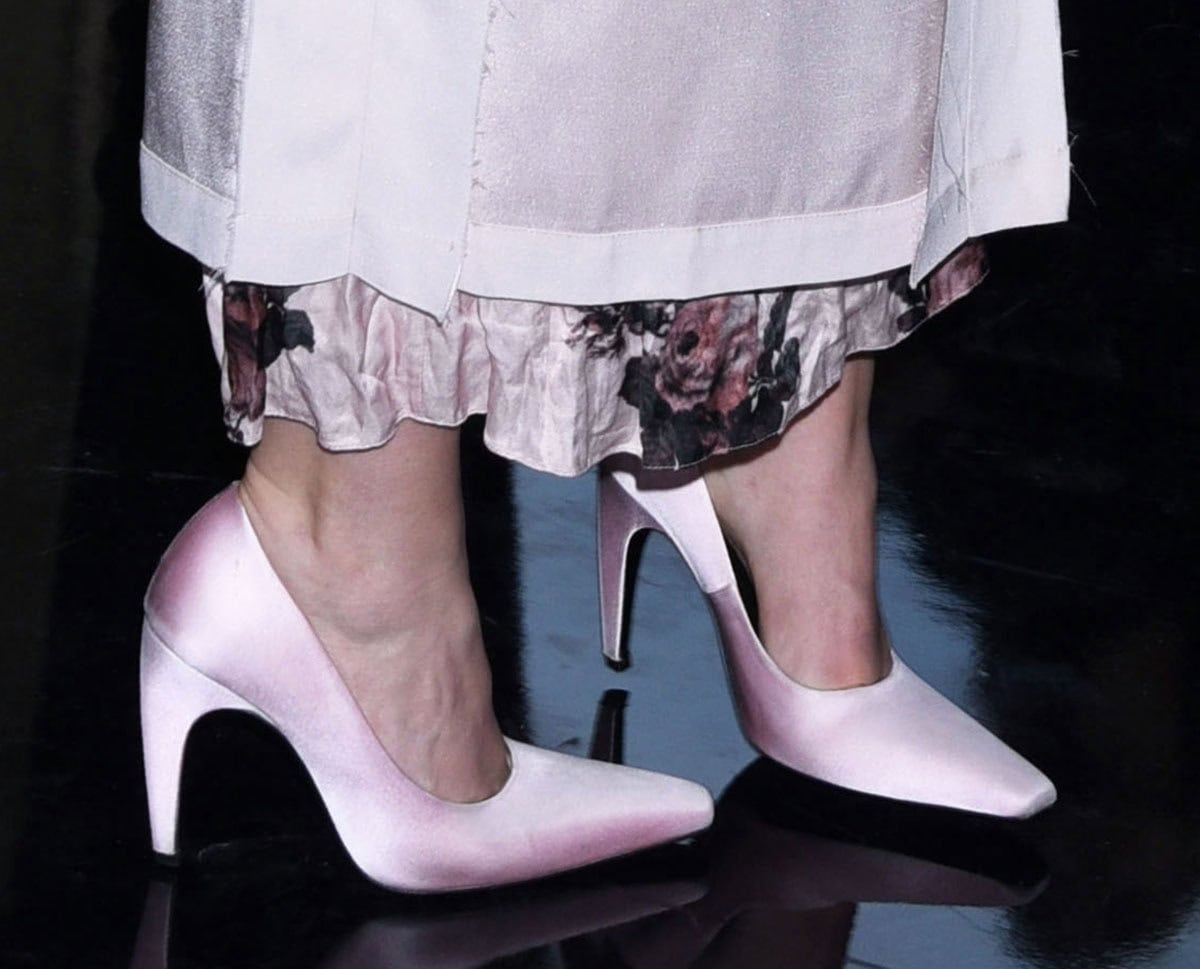 Eve Hewson embraces feminine glamour with the pink satin Jude “Fame” pumps featuring an elongated square toe and curved dagger-shaped heels