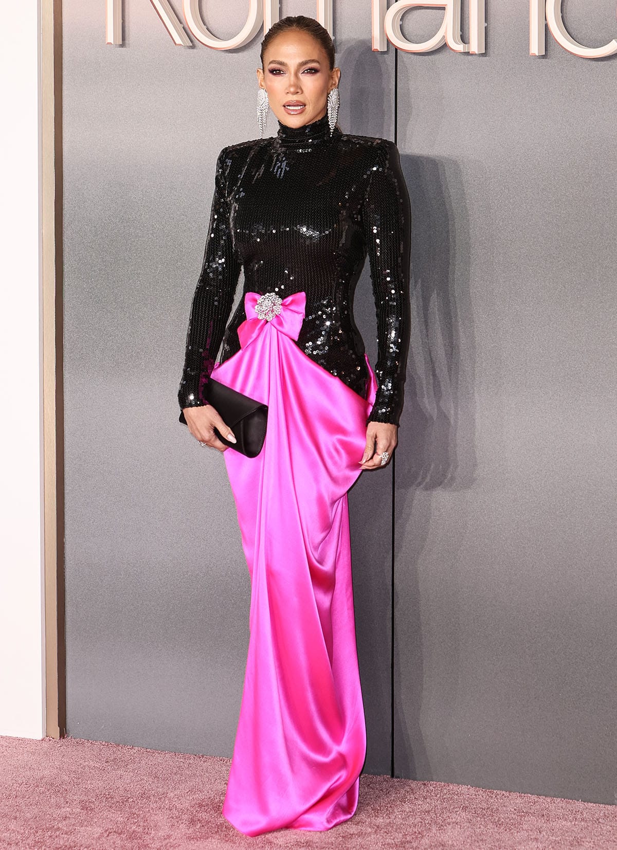 Jennifer Lopez embraces Barbiecore in a black sequined long-sleeved top and a hot pink satin draped skirt with a pink bow at the waist by Richard Quinn at the UK premiere of Office Romance