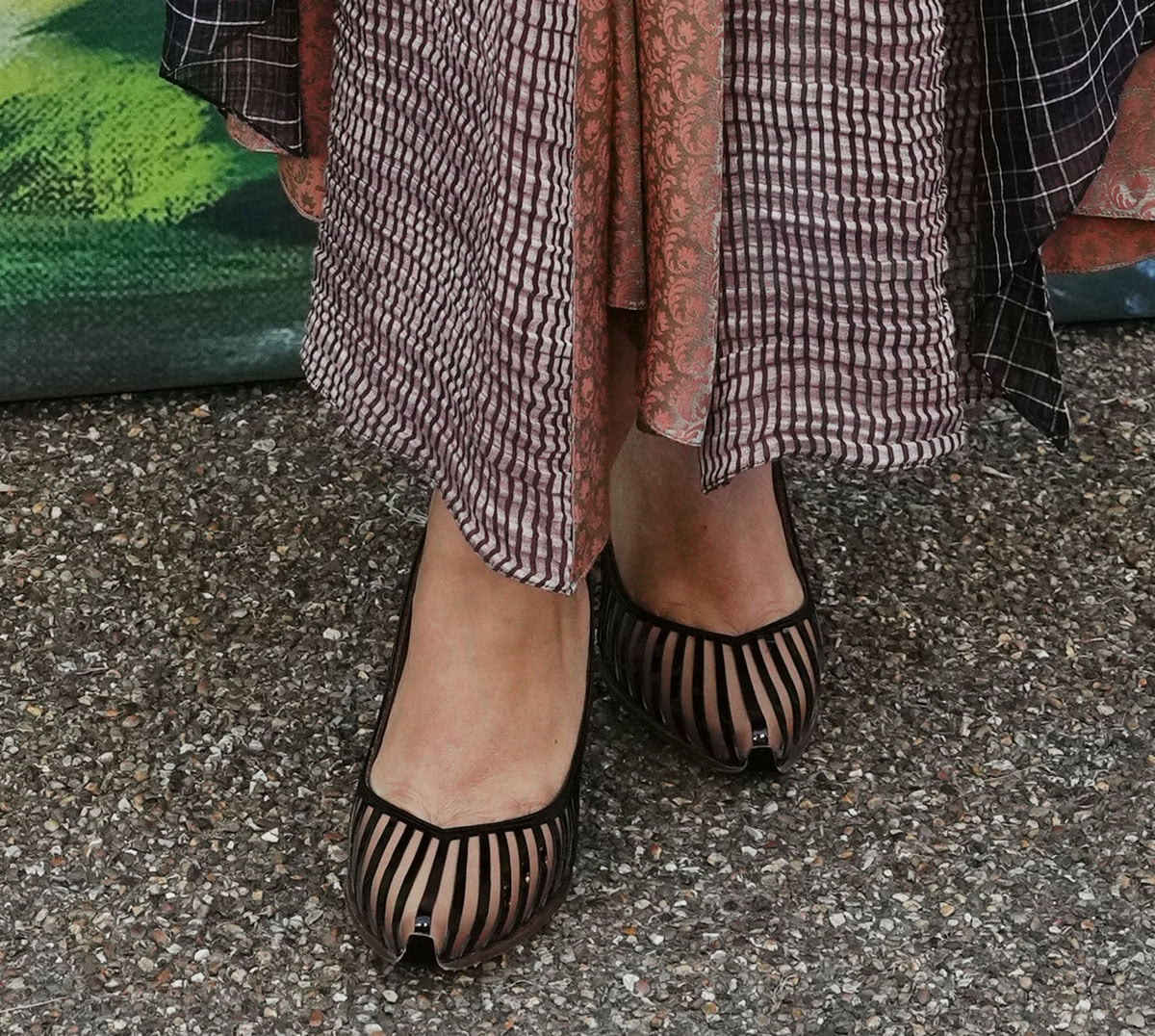 Jessie Ware wears black patent leather and sheer striped PVC pumps with pointed toes, a softly sculpted V-shaped vamp, and low stiletto heels that balance her statement ensemble