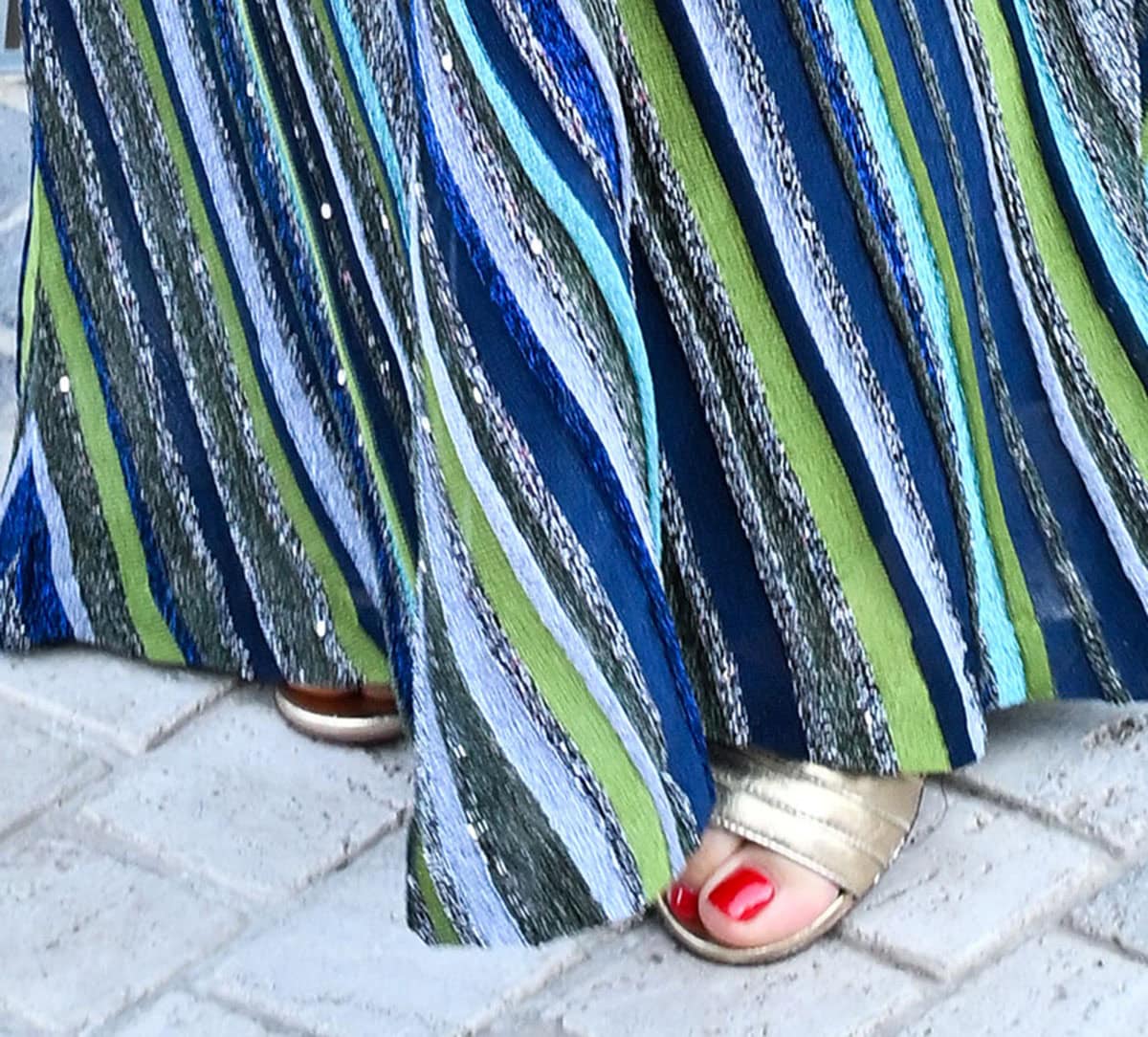 Olga Kurylenko slips her red-pedicured feet into a pair of light gold sandals with open toes and a wide front strap with horizontal stitching