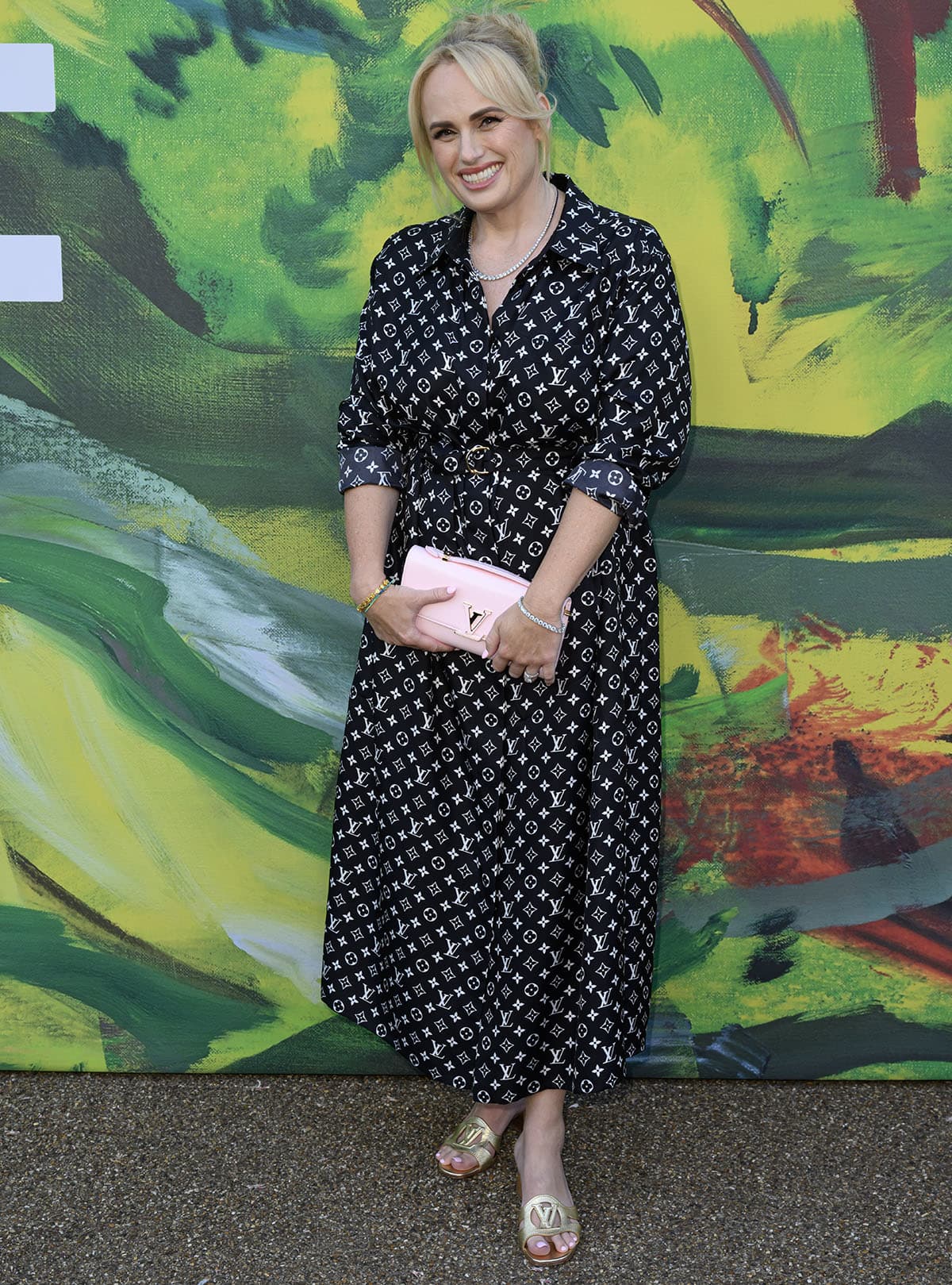 Rebel Wilson embraces logomania, teaming her gold LV mules with a black monogram silk shirt dress