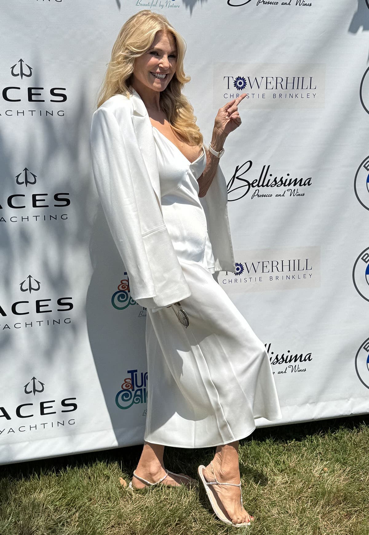 Christie Brinkley pairs her flat sandals with a breezy white slip-style midi dress, styled with a draped white blazer