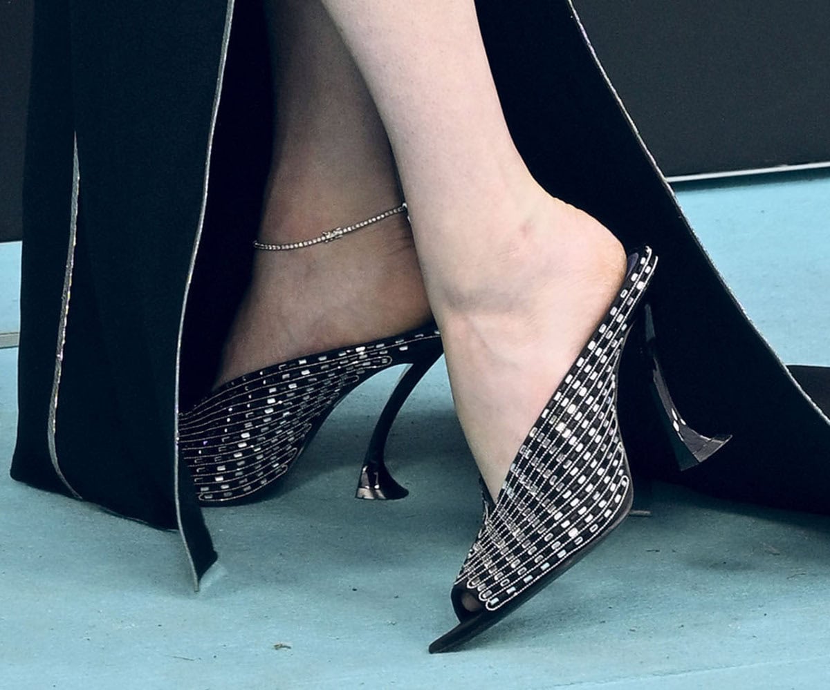 Haley Bennett shines in her striking Lanvin “Midnight Step” mules featuring V-shaped vamps, peep toes, curved heels, and all-over crystals arranged in geometric grid lines