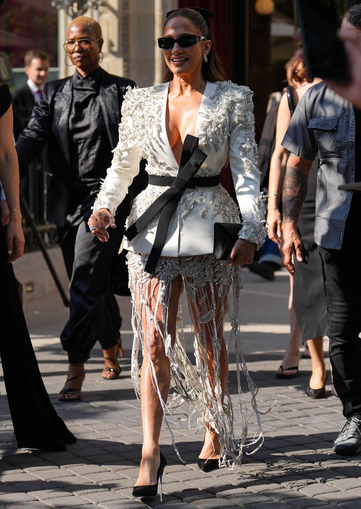 Jennifer Lopez pairs her black pumps with a jacket-and-skirt set from Zuhair Murad’s Spring 2026 Couture collection, featuring a sculptural ivory jacket with 3D frosted beadwork and crystal embellishments, a black half-bow belt, and a heavily encrusted, semi-sheer miniskirt with crystal fringes