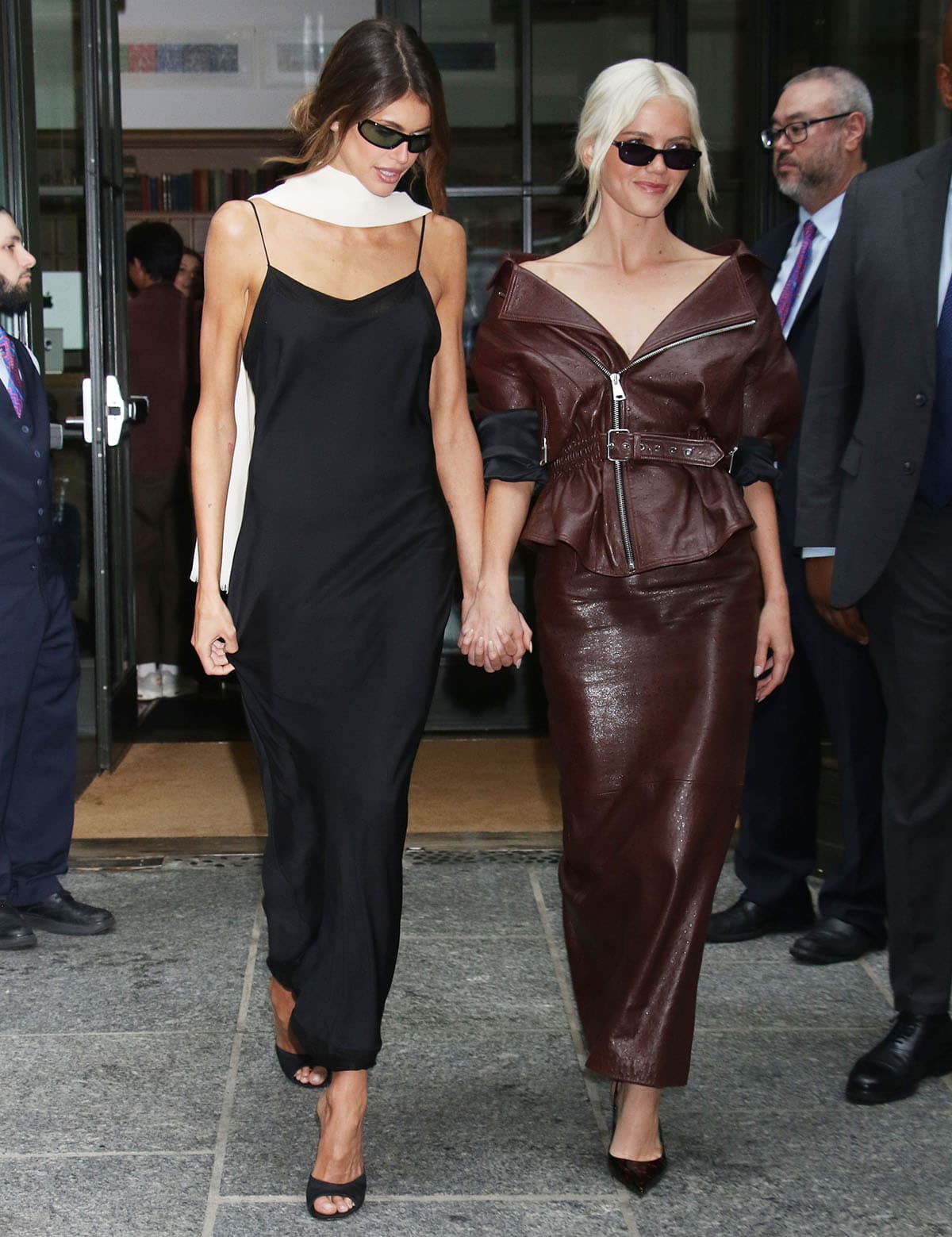 Kaia Gerber channels Carolyn Bessette-Kennedy’s ’90s minimalism in a black satin slip dress and ivory shawl, finishing the look with black Gianvito Rossi Sofia peep-toe mules
