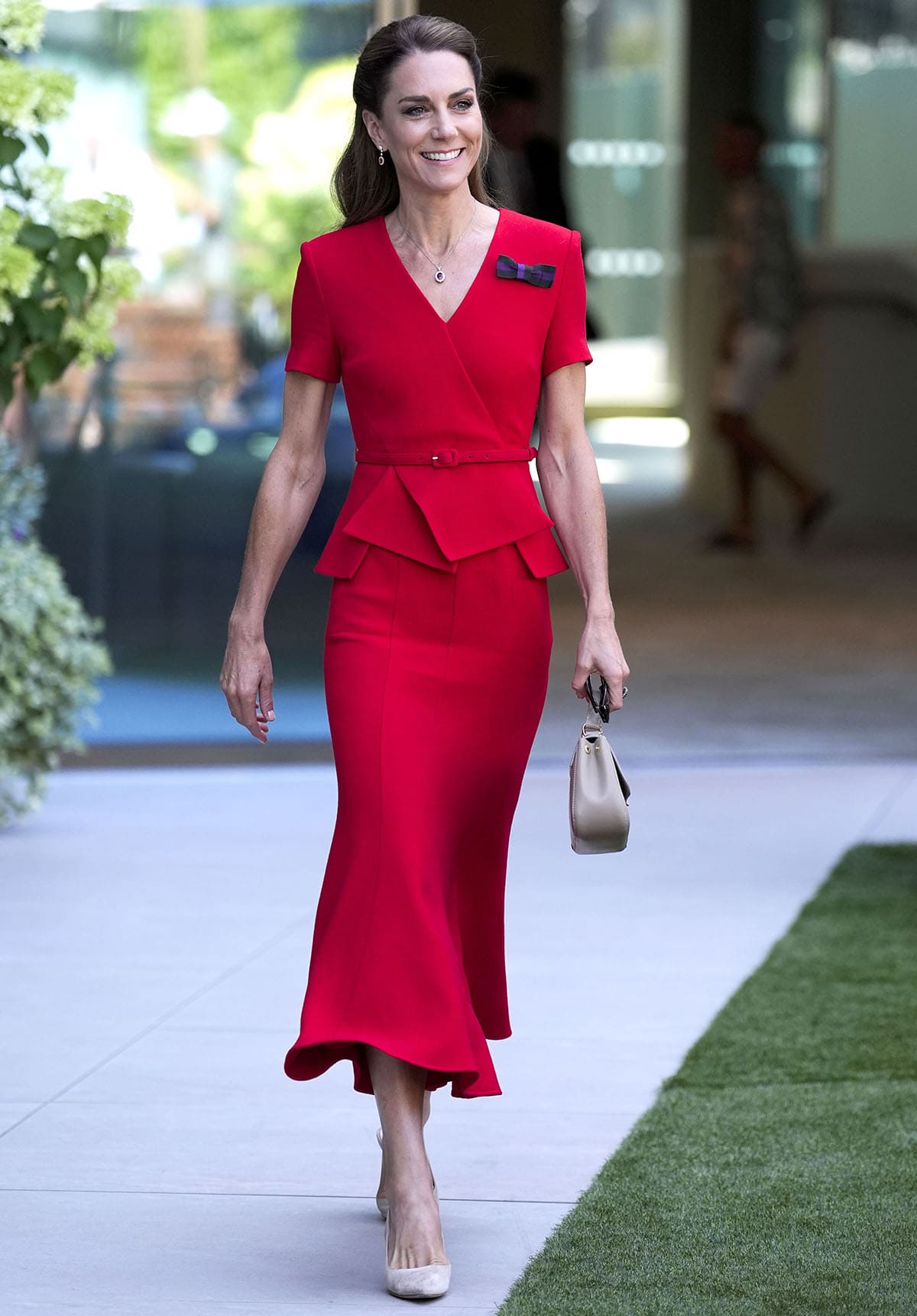 Kate Middleton pairs her versatile nude pumps with a vibrant red midi dress by Roland Mouret featuring an origami-style draped peplum and a flared midi skirt