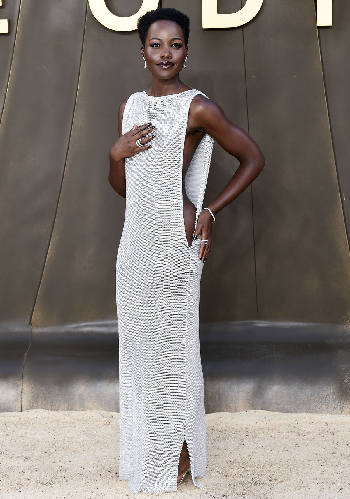 Lupita Nyong'o stuns in a crystal-embellished Christian Cowan column gown with dramatic side cutouts, styled with mirrored silver Aquazzura "So Nude" sandals at The Odyssey London premiere