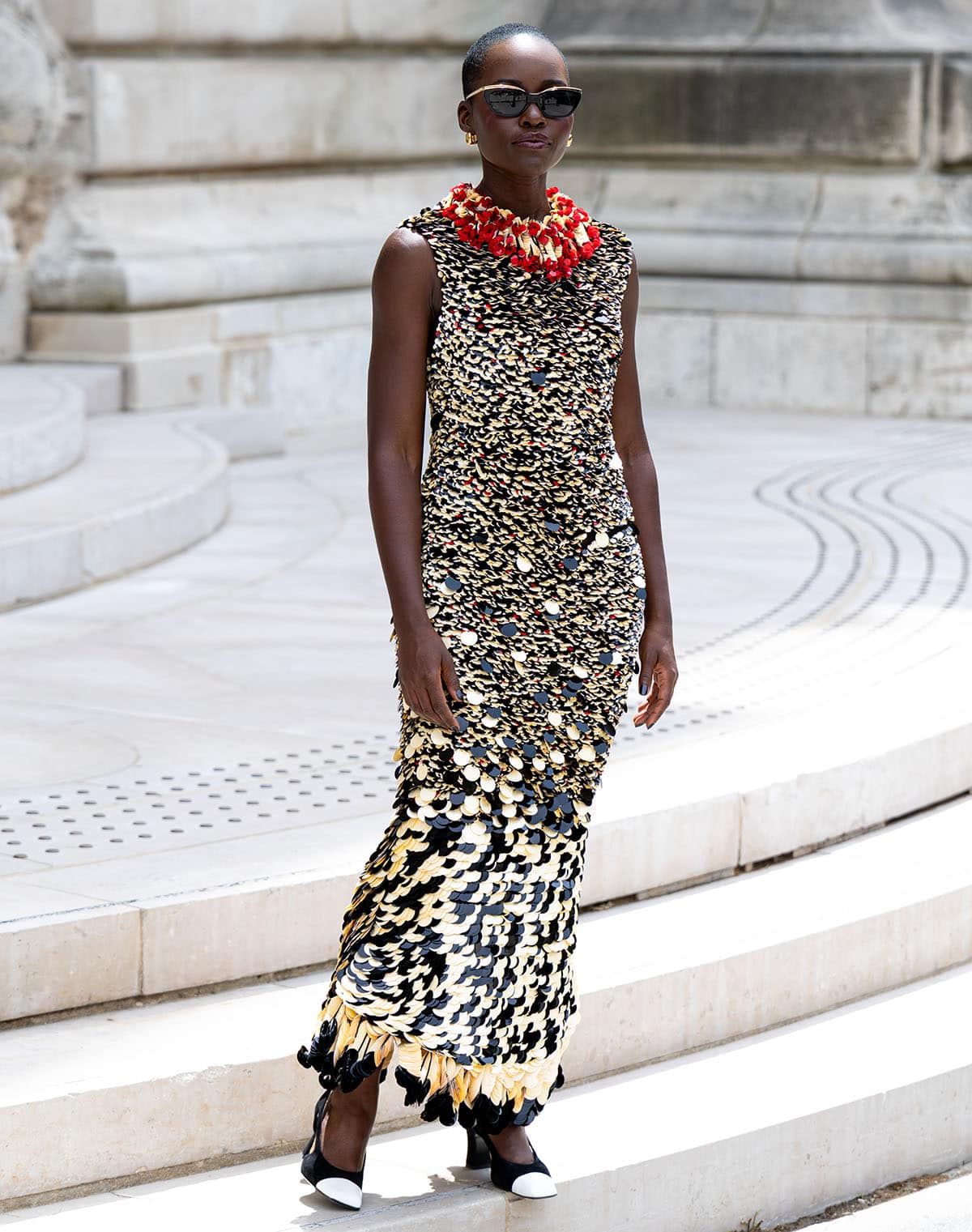 Lupita Nyong'o pairs her two-tone pumps with a sleeveless, ankle-length column dress, entirely embellished with cream, black, and red paillettes