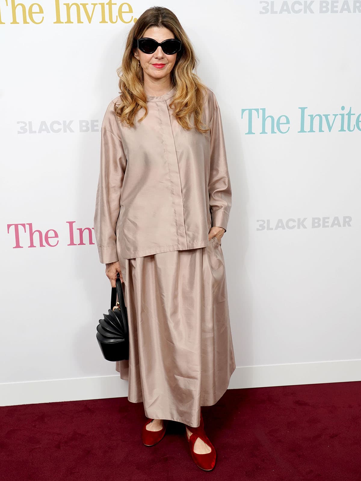 Marisa Tomei teams her red flats with a champagne pink satin set by 'S Max Mara, featuring a boxy long-sleeved blouse and a softly pleated maxi skirt