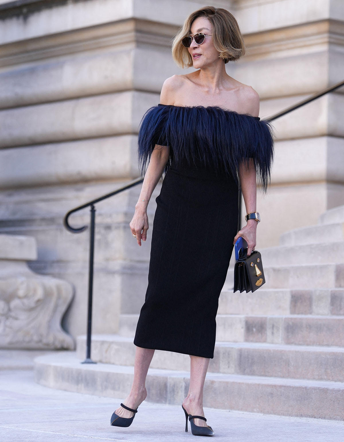 Michelle Yeoh pairs her chic and comfy mules with a Schiaparelli LBD featuring navy goat-hair trim across the strapless neckline