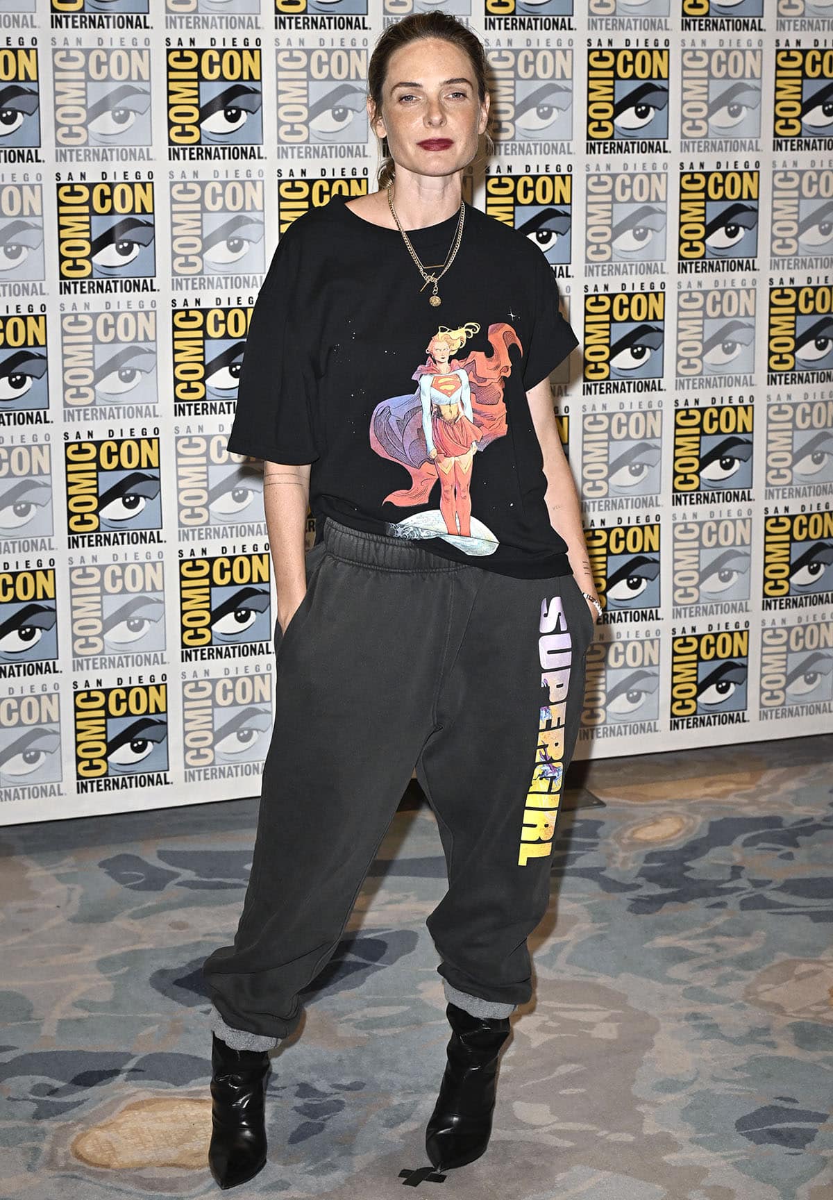 Rebecca Ferguson pairs slouchy black pointed-toe leather boots with an oversized Supergirl graphic T-shirt and charcoal sweatpants from David Koma's Supergirl capsule collection