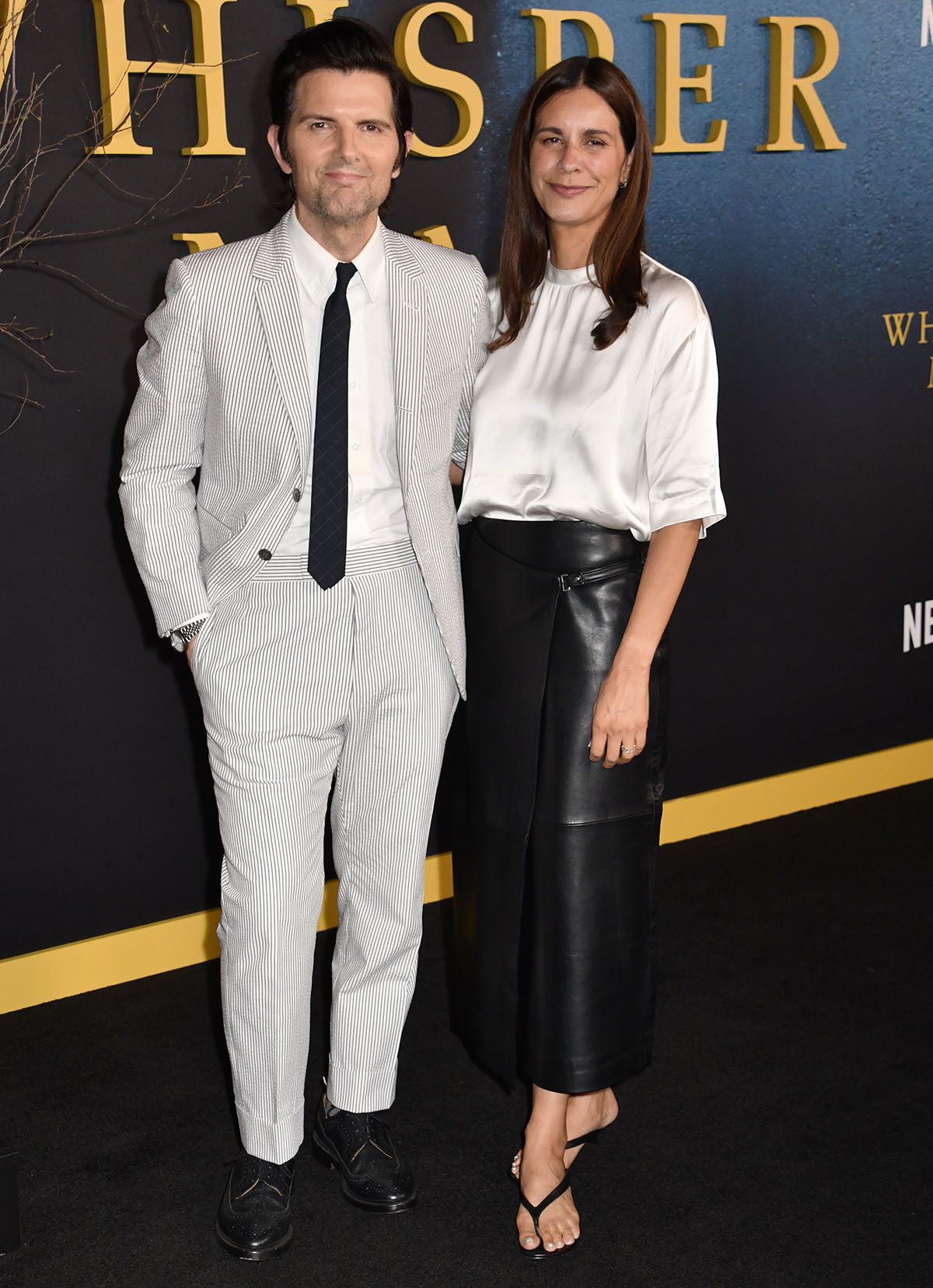 Naomi Scott, with her husband Adam Scott, showcases an effortless, contemporary look wearing a loose white satin blouse with a black leather St. Agni wrap midi skirt