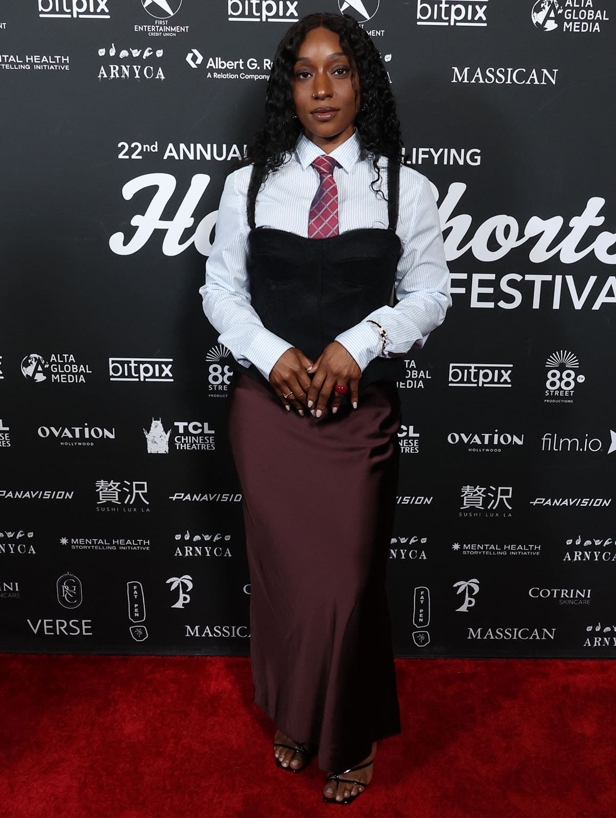 Bianca Atterberry pairs her minimalist sandals with a layered ensemble, including a light blue pinstriped collared shirt, a burgundy tie, a matching column skirt, and a black corset bustier
