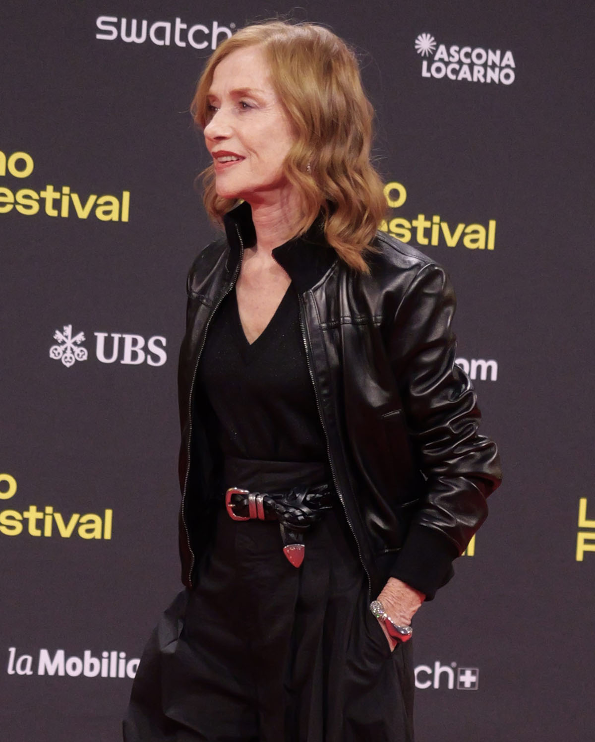 Isabelle Huppert styles her edgy, all-black look with a chunky bangle, a wavy hairstyle, and minimal makeup